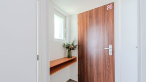 A hallway with a wooden door, a small window, and a shelf with a vase of flowers. - Le Petit (Bratislava)