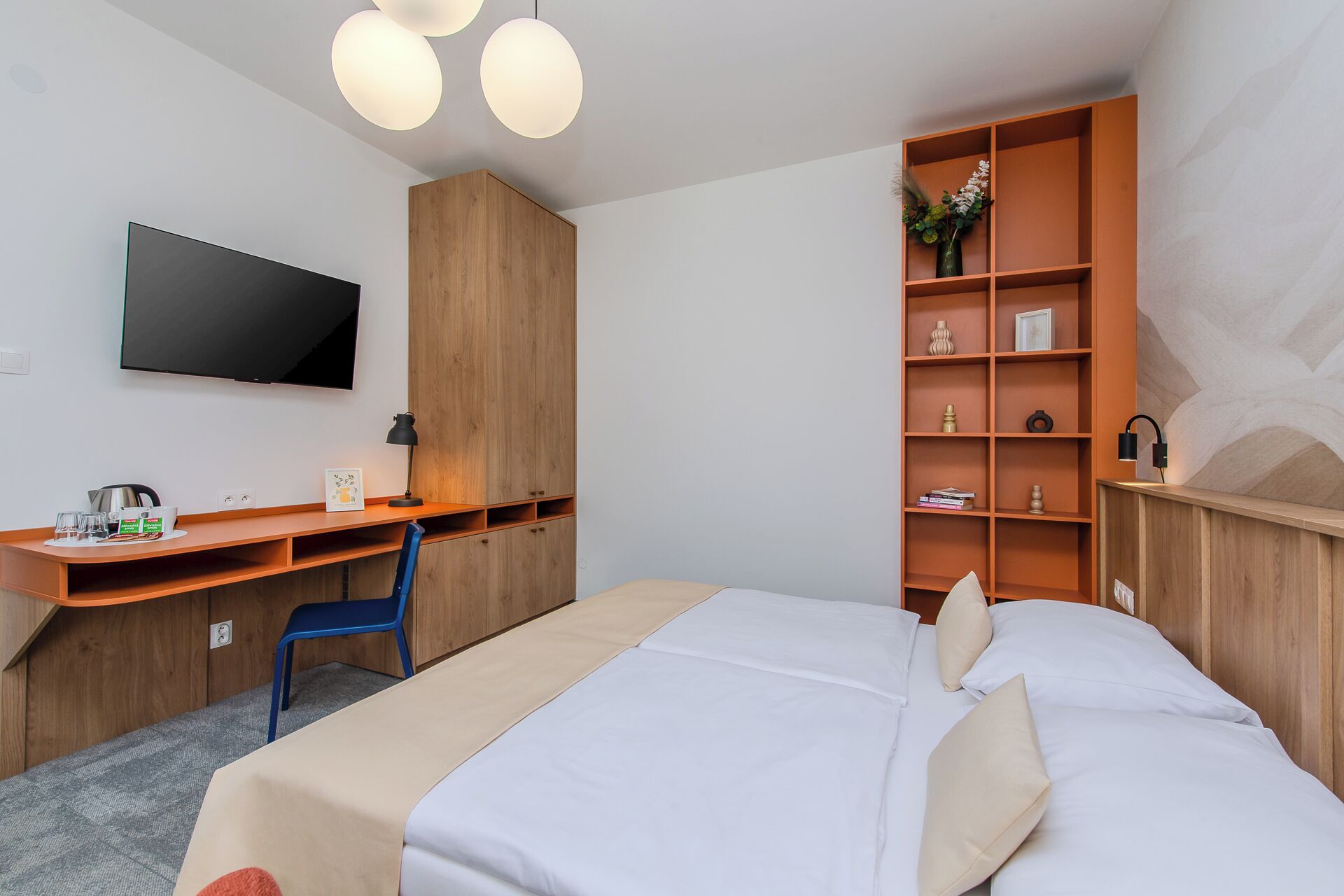 A hotel room with a bed, a desk, a chair, a television, and a bookshelf.
