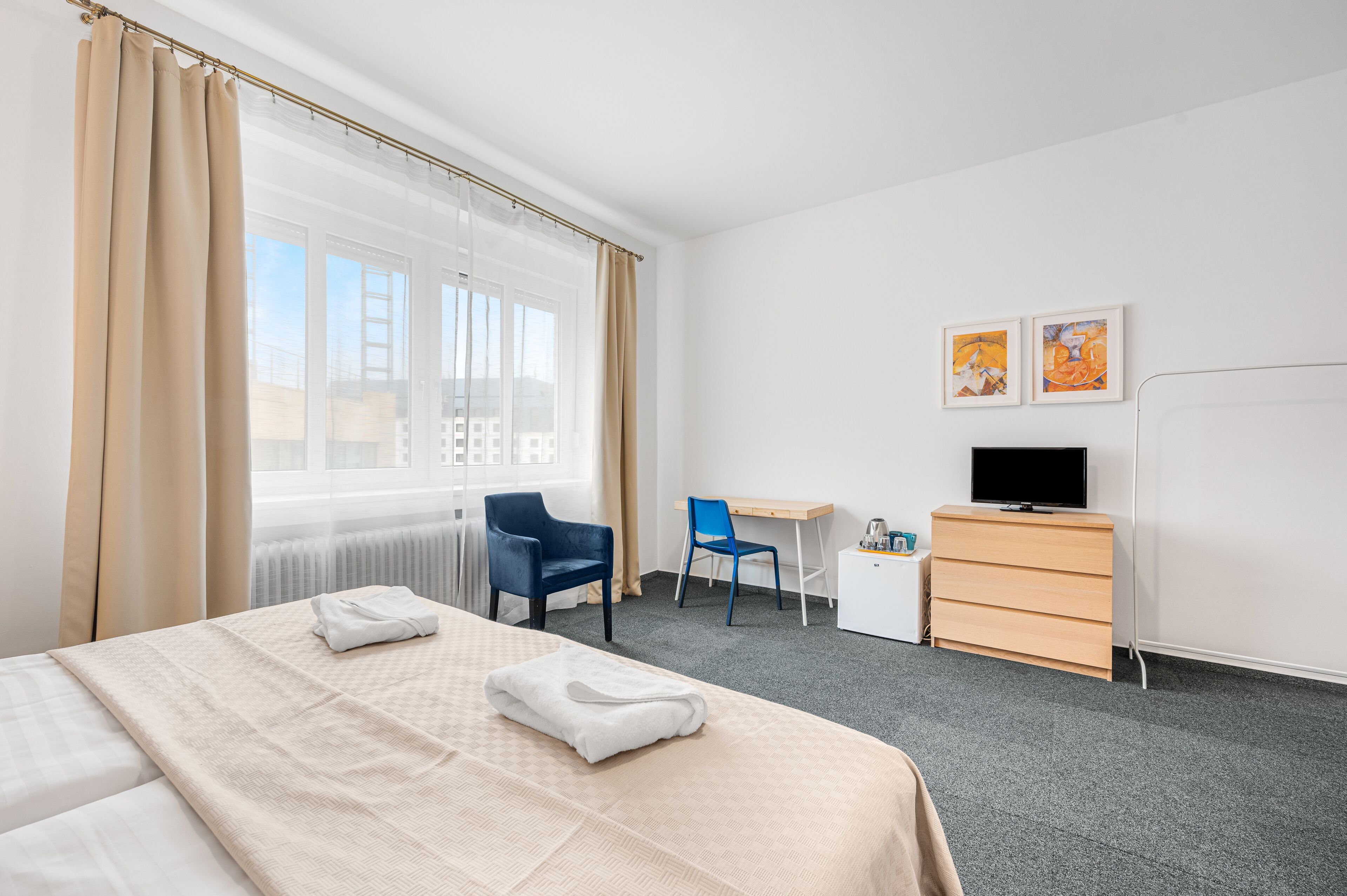 Una habitación de hotel con cama, escritorio, silla, televisor y cómoda.