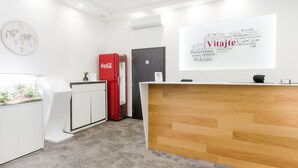 A reception area with a wooden reception desk, a red Coca-Cola refrigerator, a world map clock, and a wall with multilingual welcome signs. - Le Petit (Bratislava)