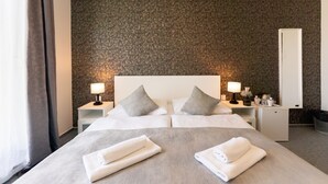 A hotel room with two beds, a small desk, a nightstand with lamps, and a mirror. - Le Petit (Bratislava)