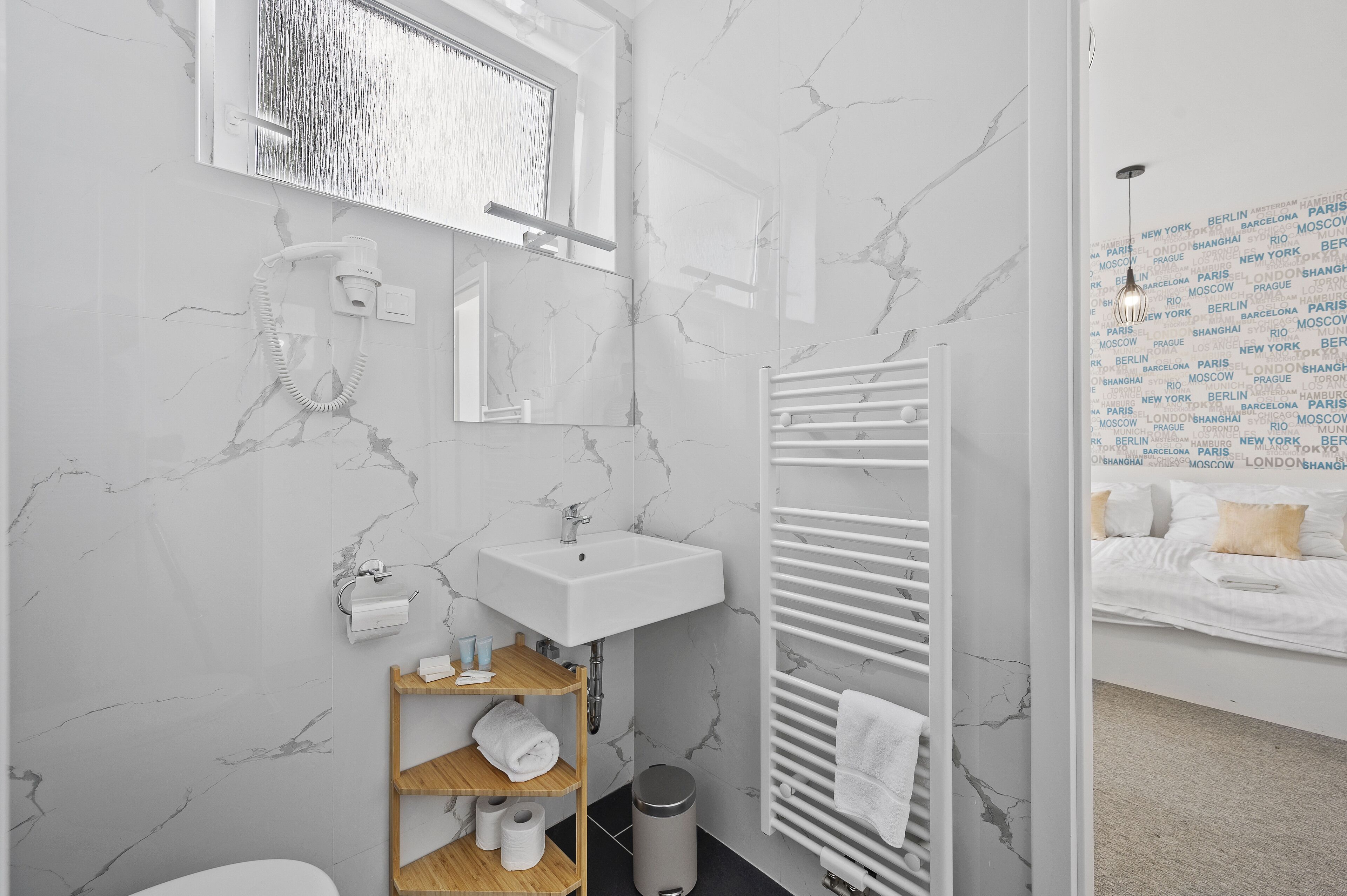 Un bagno moderno con zoccolo in marmo, lavandino bianco, porta asciugamani e zona doccia.