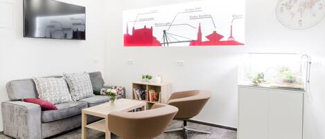 A modern living room with a grey sofa, two armchairs, a coffee table, and a TV mounted on the wall.