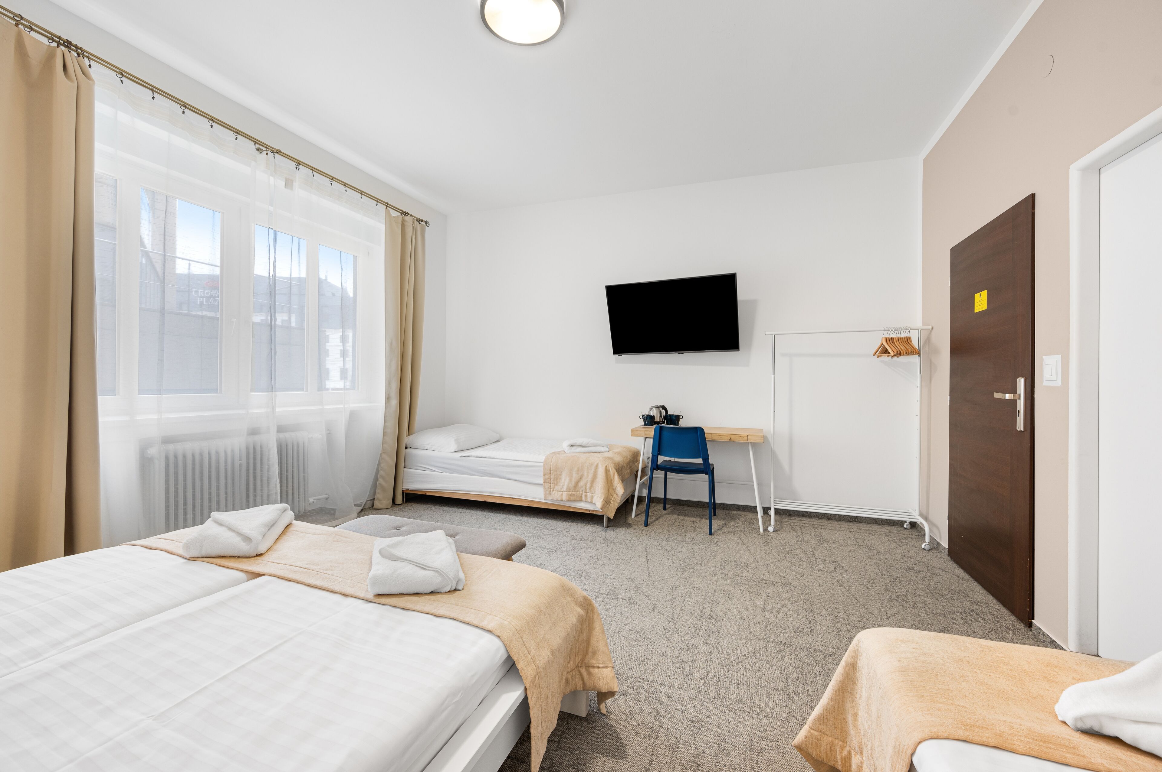 Una habitación de hotel con dos camas, un escritorio, una silla, un televisor y una puerta.