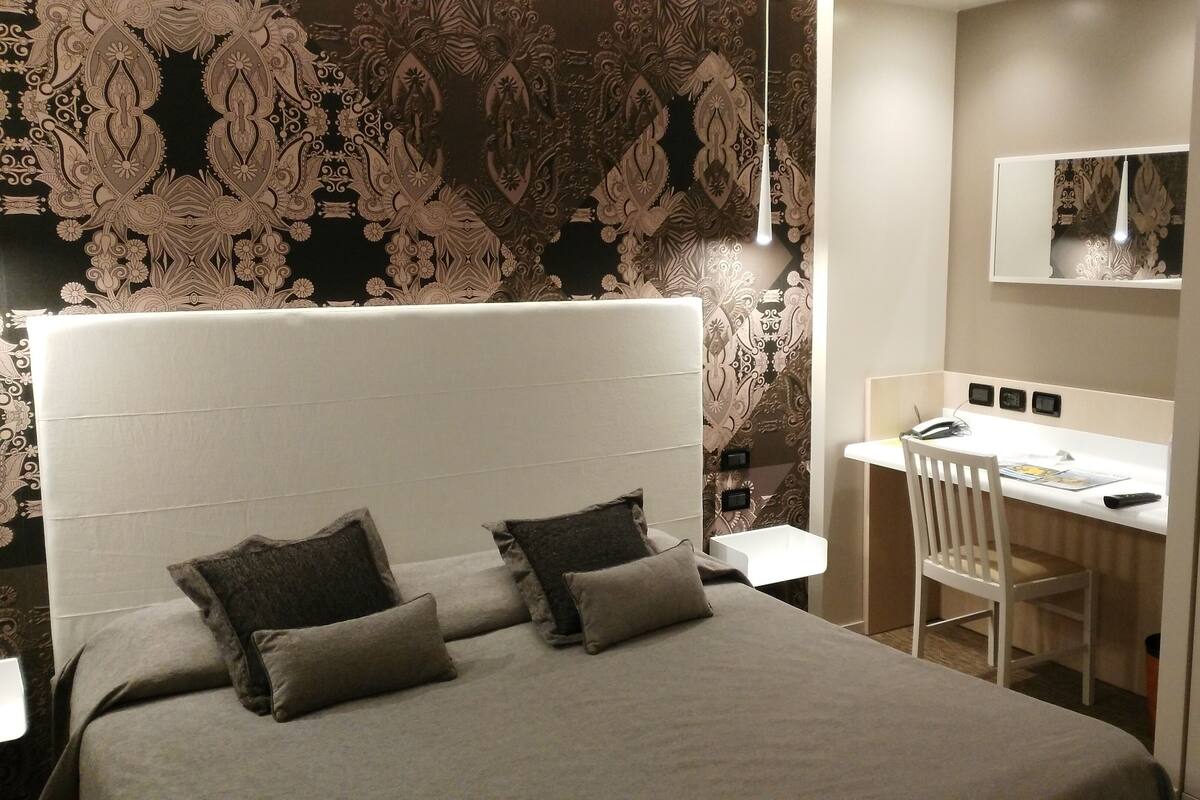 A modern bedroom with a large bed, two pillows, a desk, and a chair.