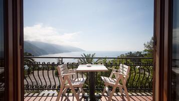A balcony with two white chairs and a table, overlooking a mountainous landscape and a body of water.