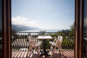 A balcony with two white chairs and a table, overlooking a mountainous landscape and a body of water.