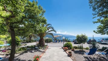 A sunny outdoor area with a paved walkway, lounge chairs, and a view of the sea.