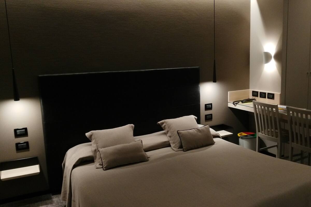 A modern bedroom with a large bed, bedside tables, a desk, and a wardrobe.