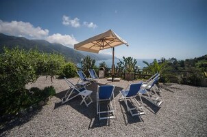 Una terraza con tumbonas y una sombrilla grande, con vistas a un paisaje montañoso.