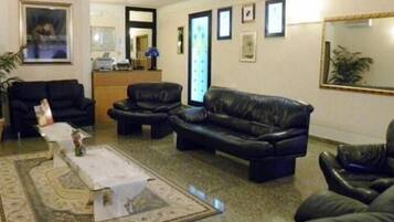 Una sala de estar con un sofá, sillones y una mesa de centro. Hay un escritorio con una computadora y un espejo en la pared.