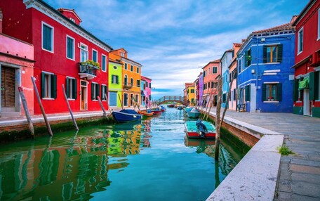 A canal with colorful buildings on either side and a wooden bridge in the distance.