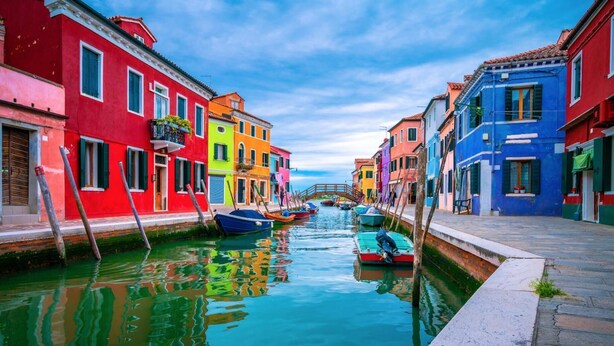 A canal with colorful buildings on either side and a wooden bridge in the distance. - Hotel Amba Alagi (Mestre)