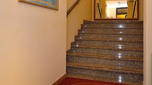 A hotel entrance with a marble staircase, a red doormat with a logo, a framed map on the wall, and wall-mounted lights. - Hotel Amba Alagi (Mestre)