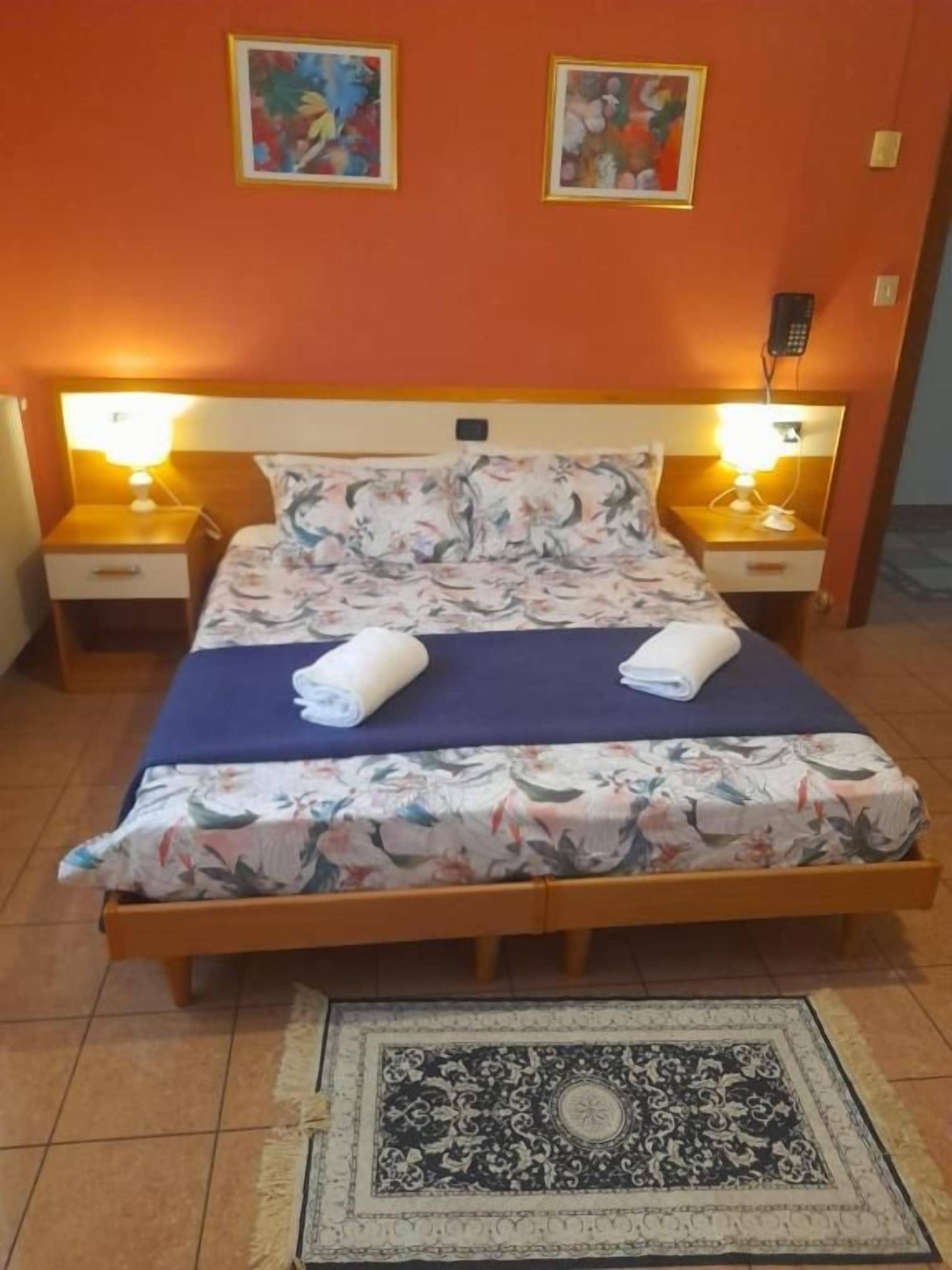 A bed with floral bedding, two bedside lamps, and a patterned rug on a tiled floor.