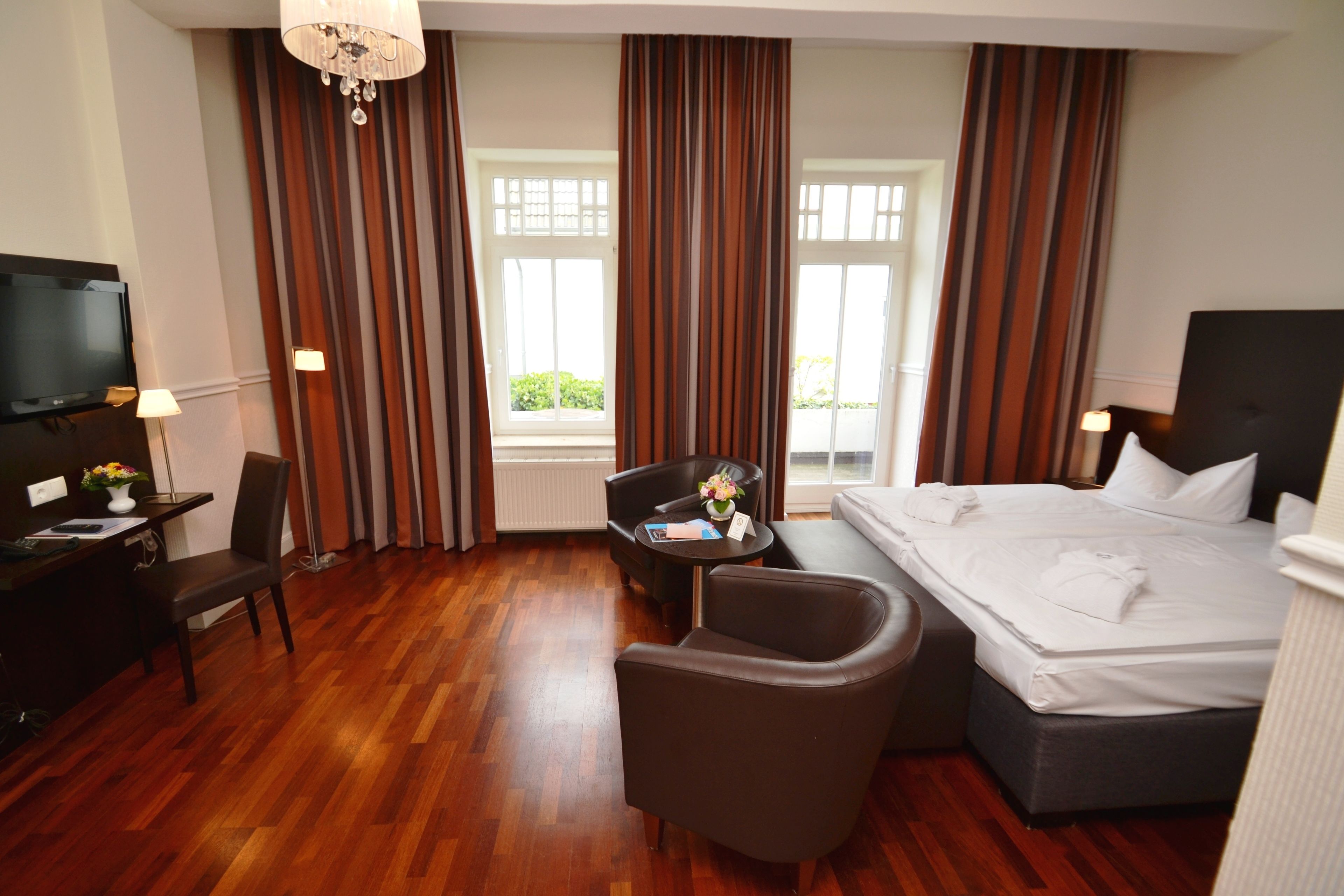Ein Hotelzimmer mit Bett, Schreibtisch mit Stuhl, kleinem Tisch und Blumenvase sowie einem Fernseher.