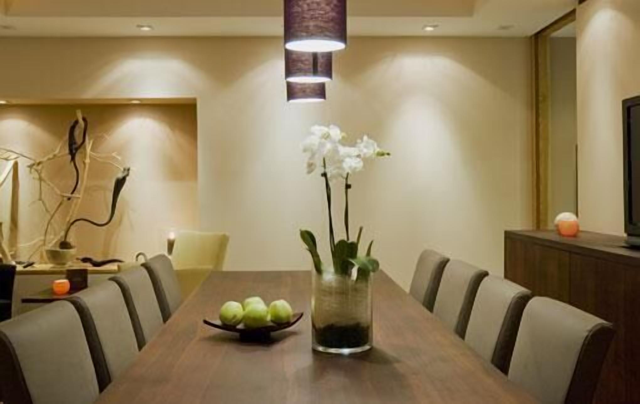 A dining area with a long table, chairs, a vase with flowers, and a decorative piece on the wall.
