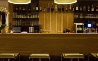 Zona de bar con mostrador de madera, estantes llenos de botellas y taburetes.