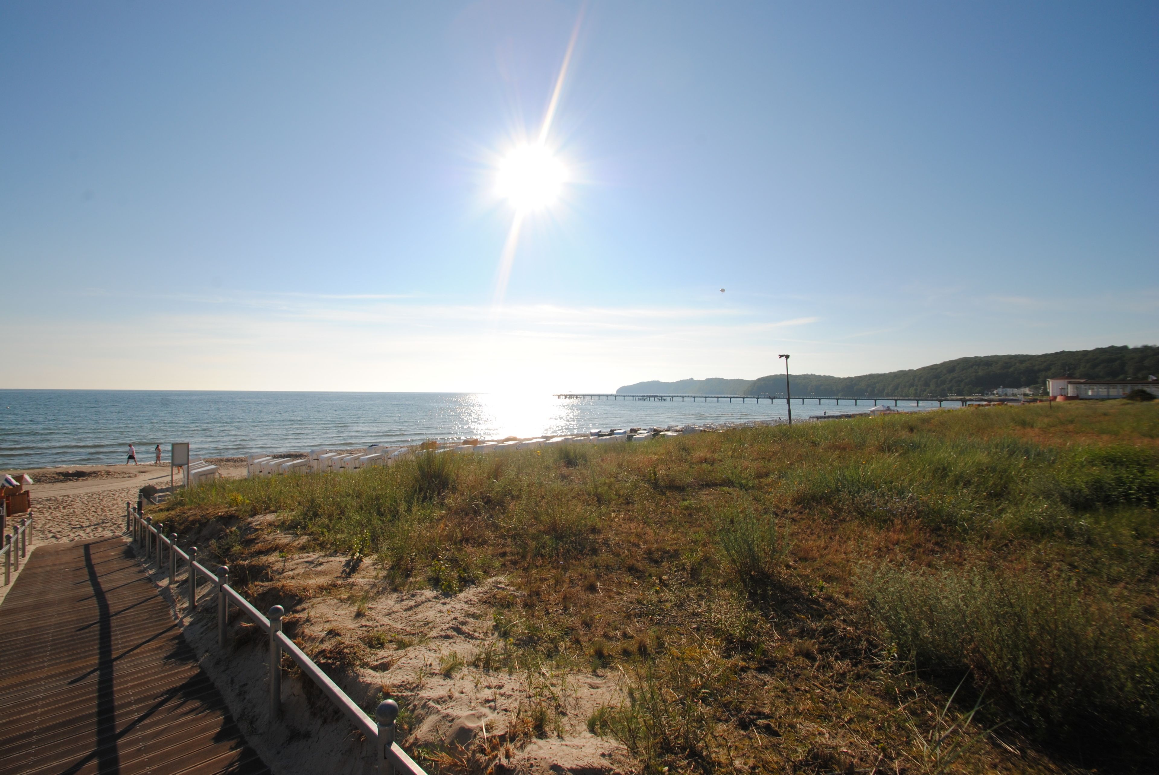 A beach with a wooden boardwalk leading to the water, a pier extending into the sea, and grassy dunes.