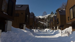 Una calle nevada con edificios modernos, cielo despejado y una montaña al fondo.