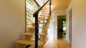 Una escalera moderna con escalones de madera y barandilla de metal, que conduce a una habitación con vistas al exterior.