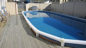 A rectangular above-ground pool with a wooden deck and a white safety railing.