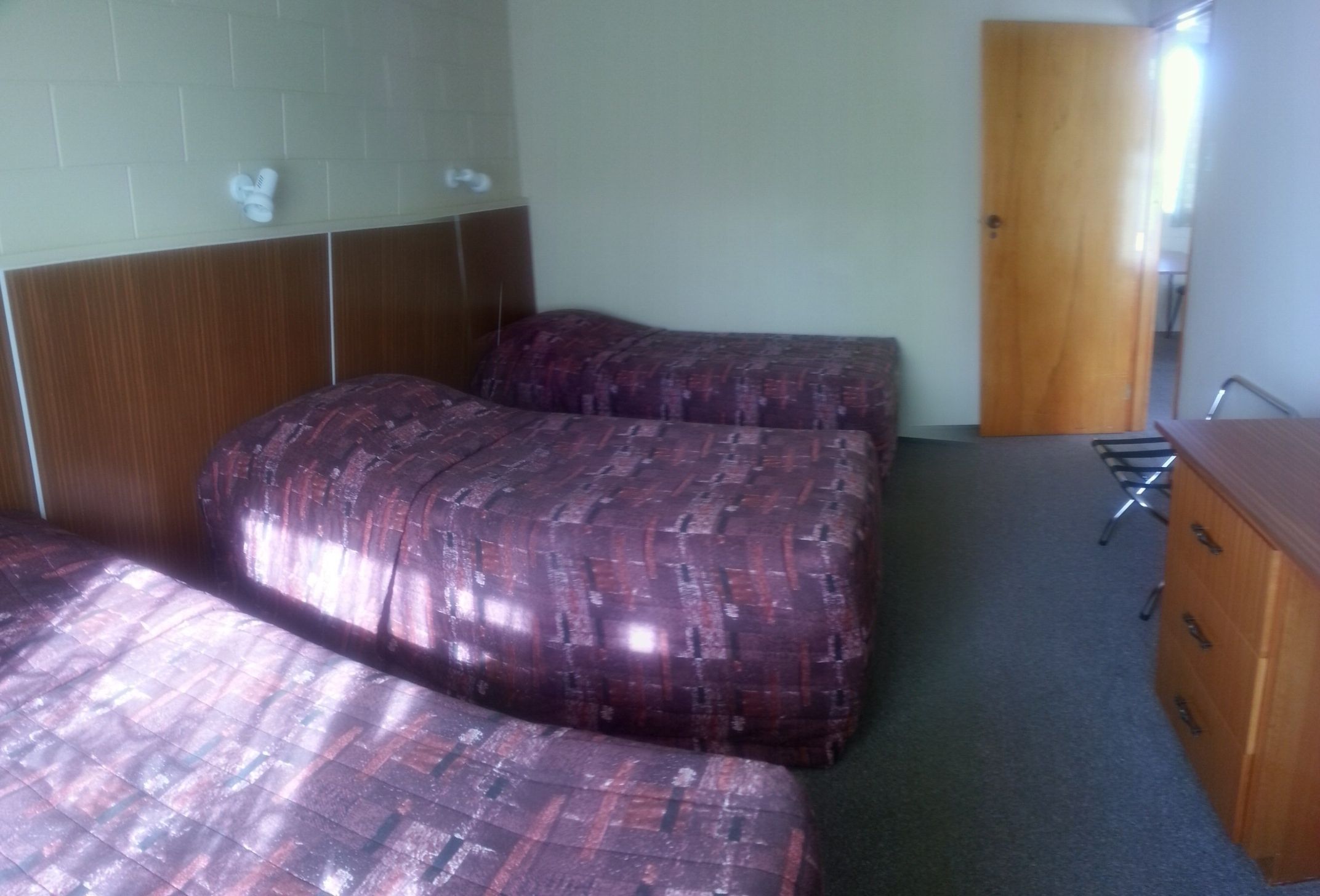 A hotel room with two beds, a wooden wardrobe, and a door.