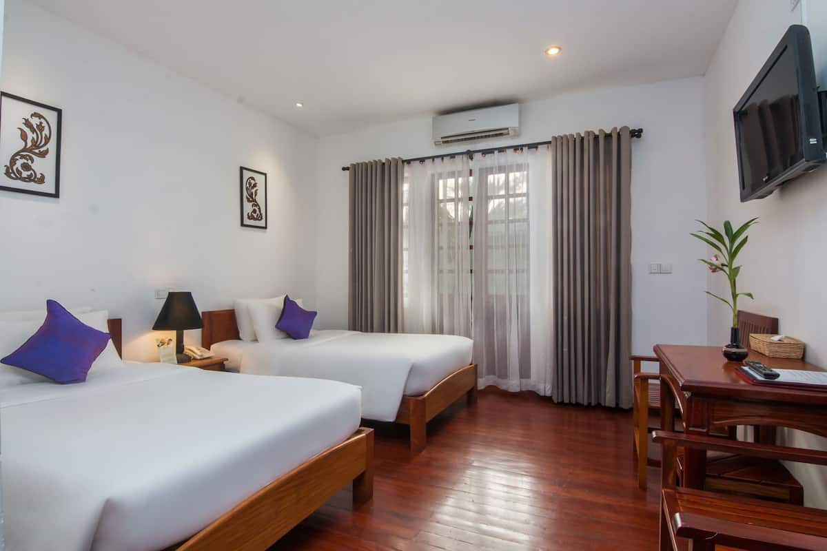 A hotel room with two beds, a desk, a chair, an air conditioning unit, and a TV on the wall.
