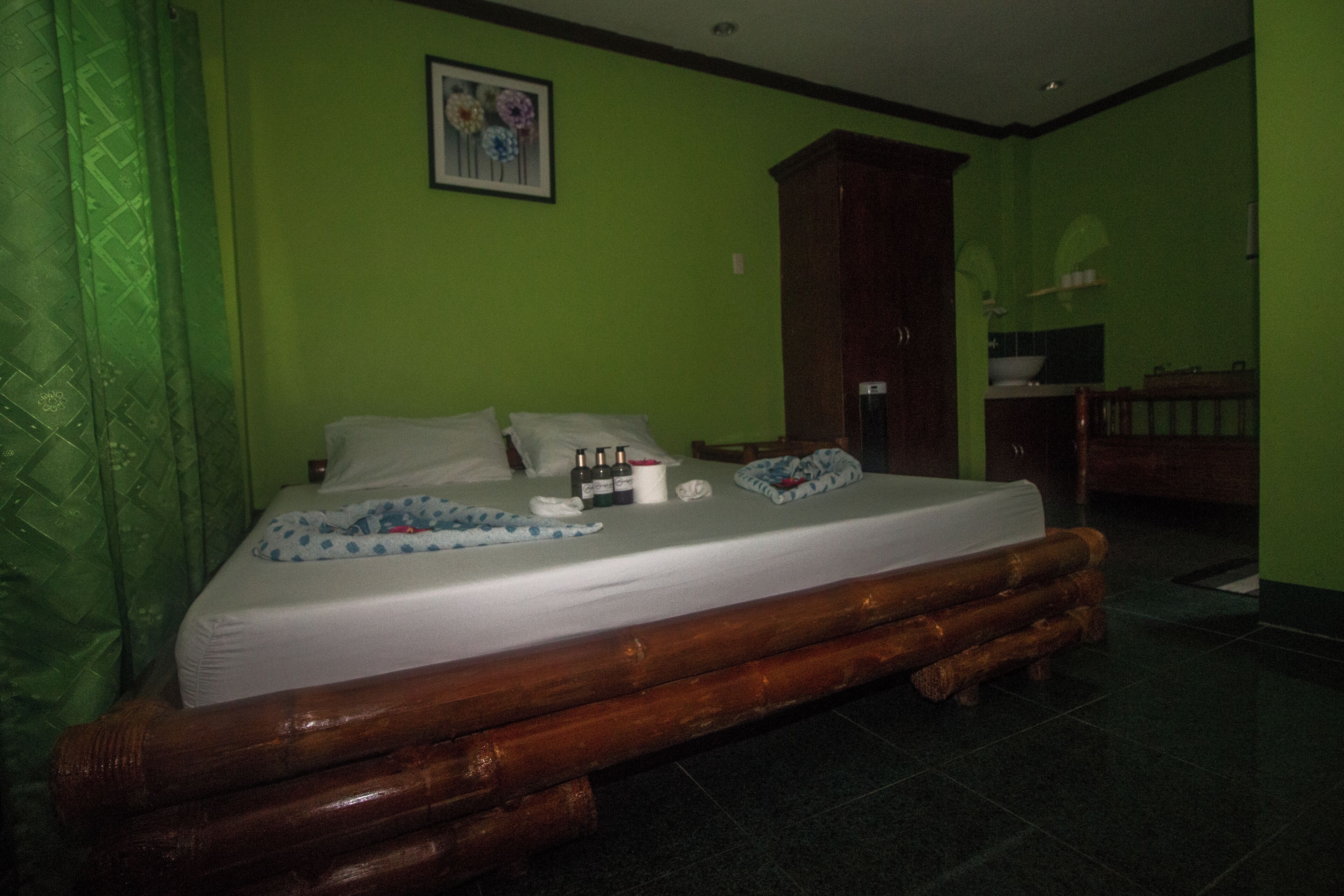 A room with a bed, a wooden headboard, a green wall, and a framed picture above the bed.