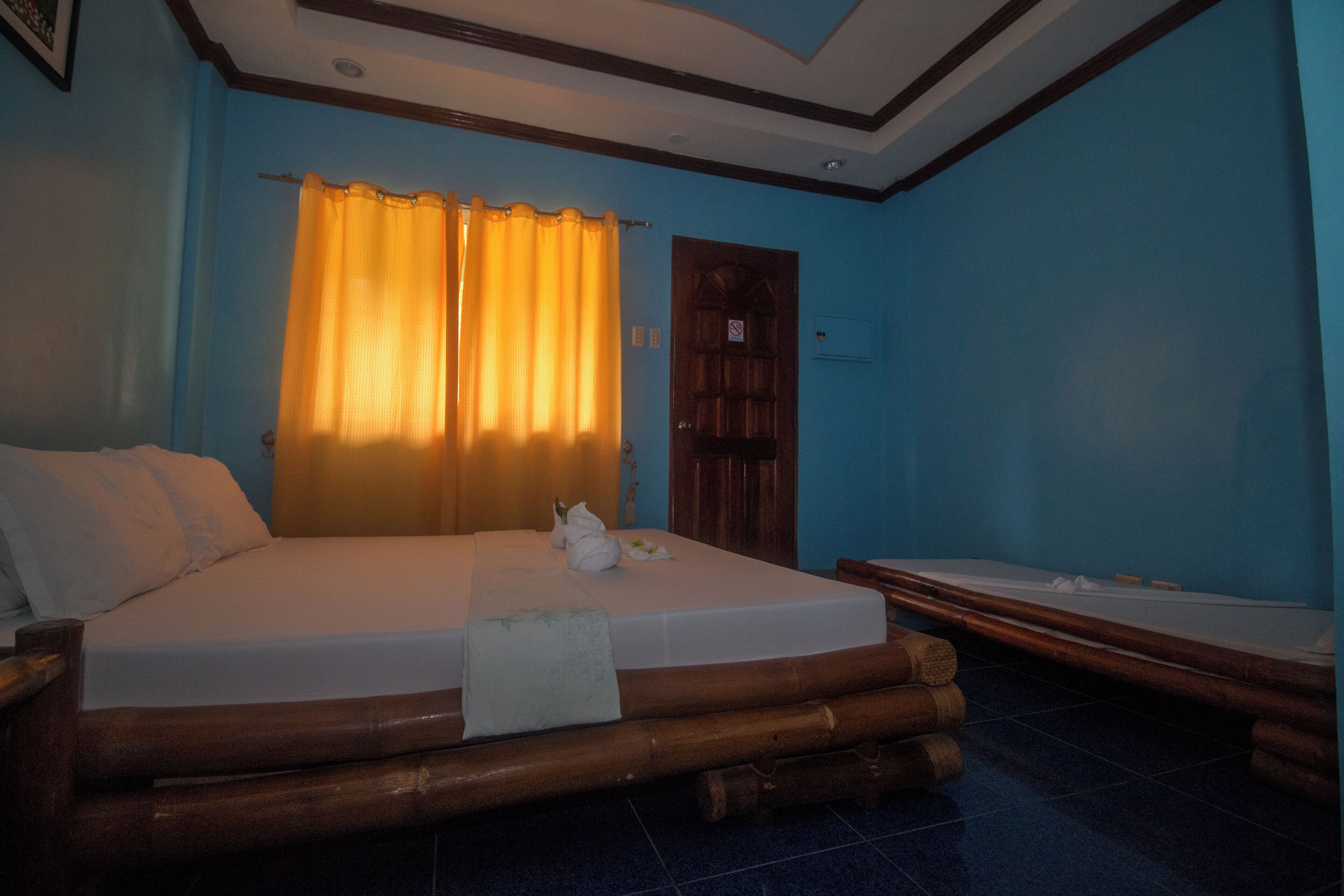 A room with a large bed, a smaller bed, a wooden headboard, and a curtain.
