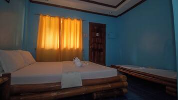A room with a large bed, a smaller bed, a wooden headboard, and a curtain.