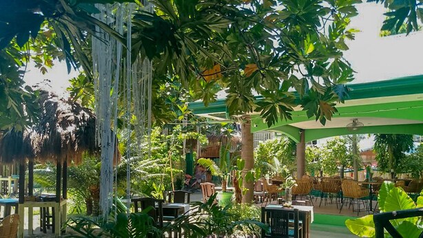 An outdoor seating area with tables and chairs, surrounded by lush greenery and a covered structure. - Moonlight Resort (Daanbantayan)