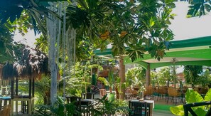 An outdoor seating area with tables and chairs, surrounded by lush greenery and a covered structure. - Moonlight Resort (Daanbantayan)