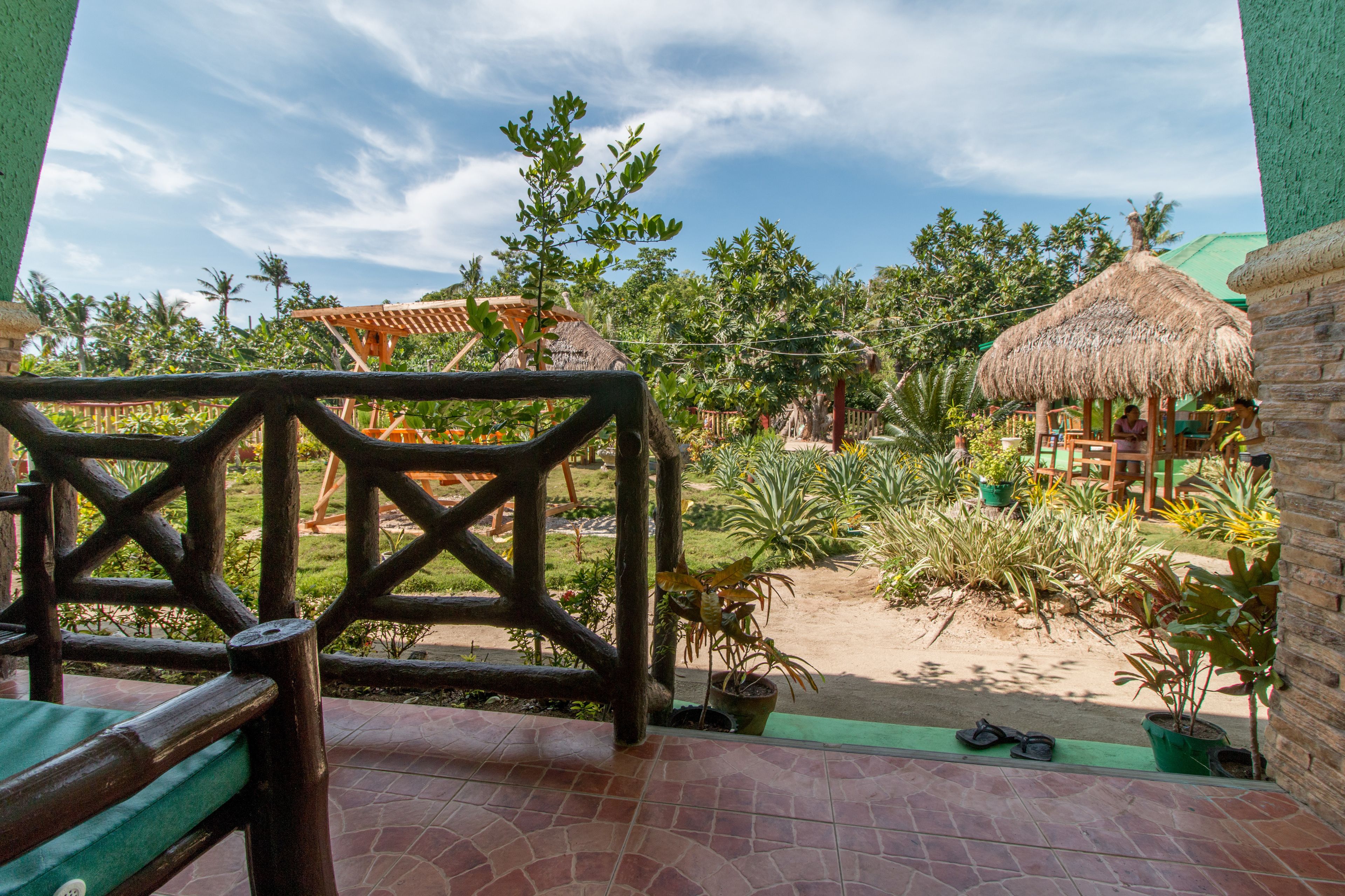A patio area with a wooden fence, potted plants, and a thatched-roof structure.