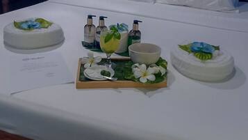 Une table blanche sur laquelle se trouve un plateau de nourriture, comprenant un gâteau décoré de motifs bleus et verts, un verre contenant une boisson et un bol. On y trouve également des bouteilles de savon pour les mains et un menu.