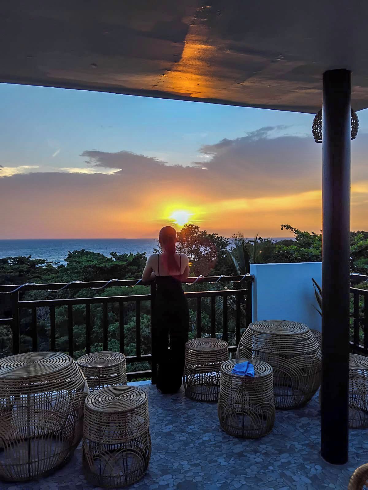 Un balcón con mobiliario de mimbre y vista al atardecer sobre el océano.