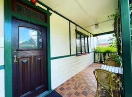 A covered porch with a wooden door, a tiled floor, and wicker furniture.