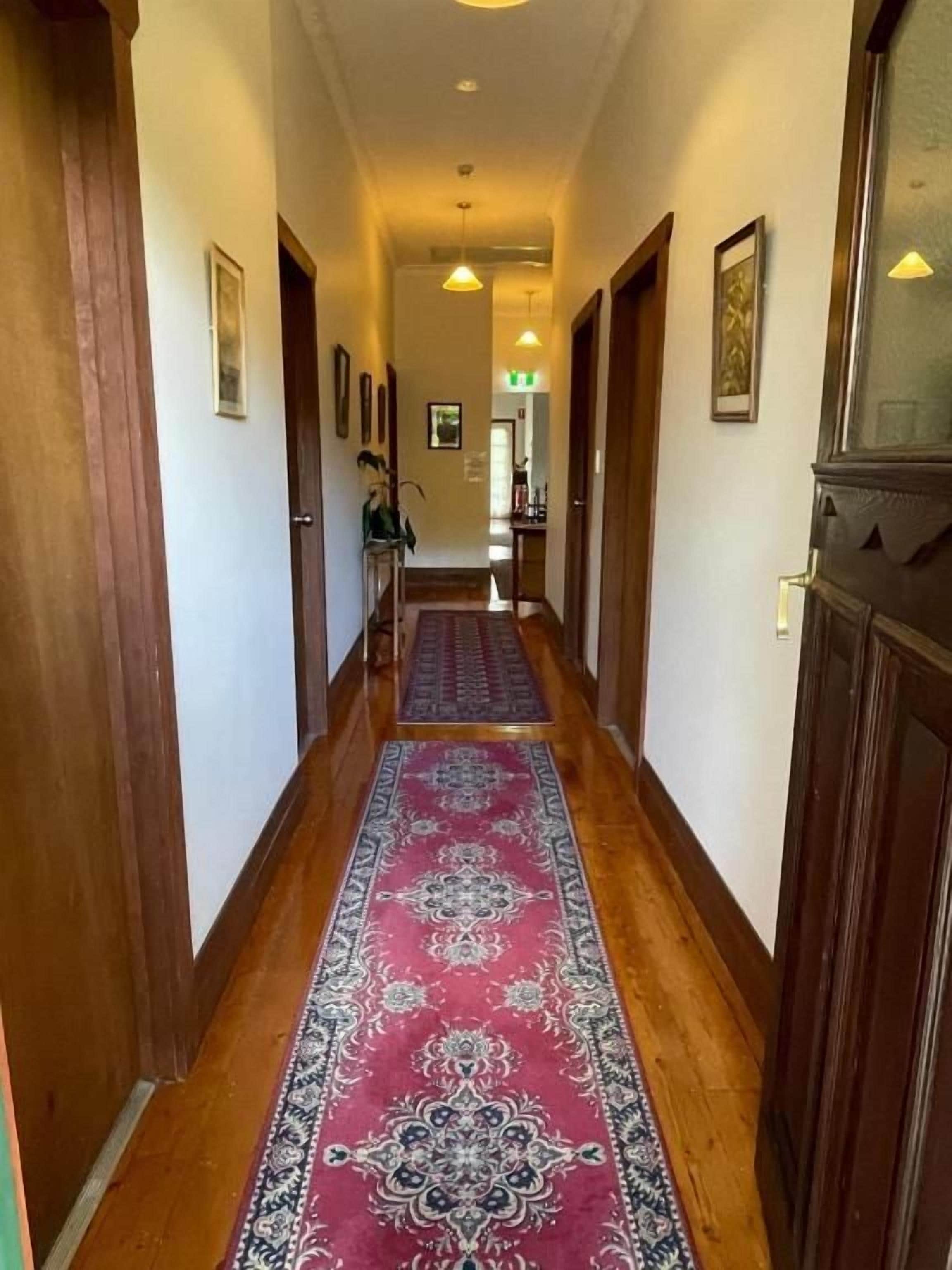 A hallway with wooden flooring, a patterned carpet, and doors on either side.