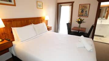 A hotel room with a large bed, bedside lamps, a desk with a chair, a vase of flowers, and a bathroom visible through an open door.