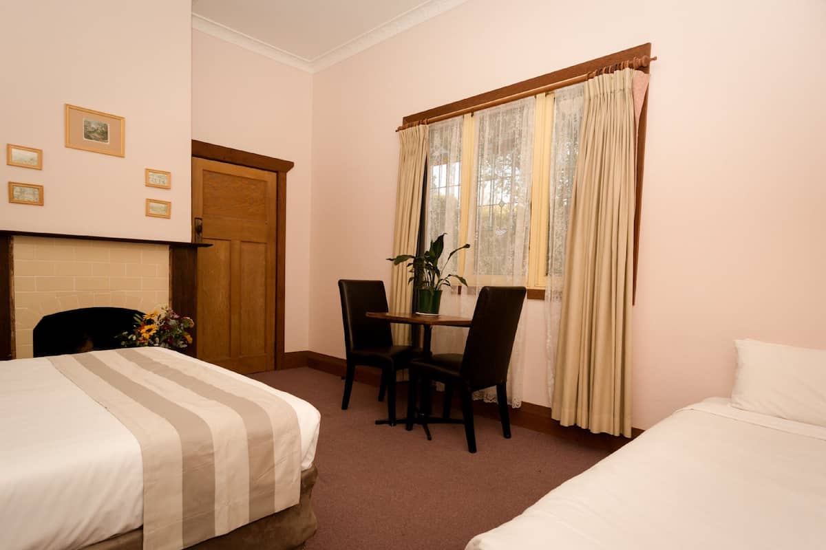 A hotel room with two single beds, a wooden table with chairs, a potted plant, and a fireplace.