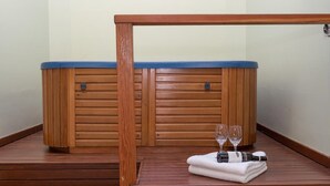 Un banco de madera con un cojín azul, una mesita con dos vasos y una botella, y una toalla.