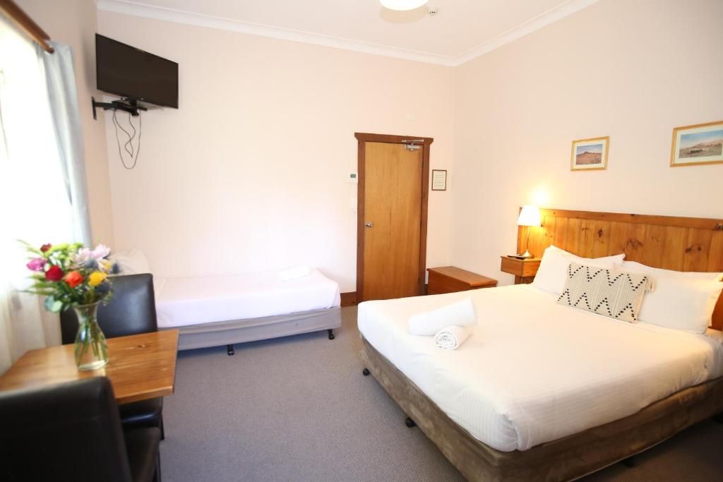 Ein Hotelzimmer mit Bett, Nachttisch, Lampe, Fernseher und einem kleinen Tisch mit Blumen.