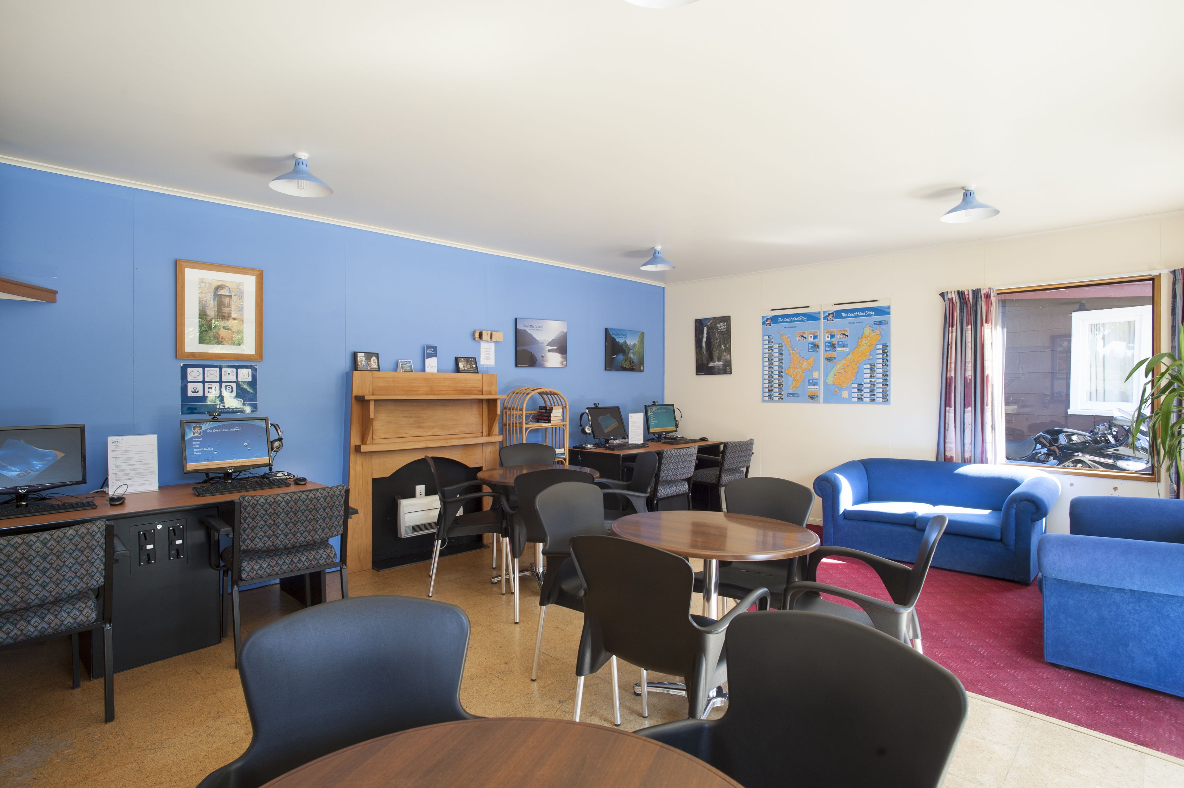 Una habitación con escritorio, ordenador, sillas, sofá azul y una ventana con cortinas.