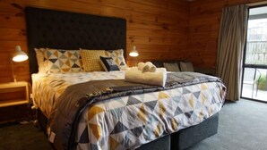 Een slaapkamer met houten lambrisering, een groot bed, beddengoed met een geometrisch patroon, twee bedlampen en een raam met gordijnen.