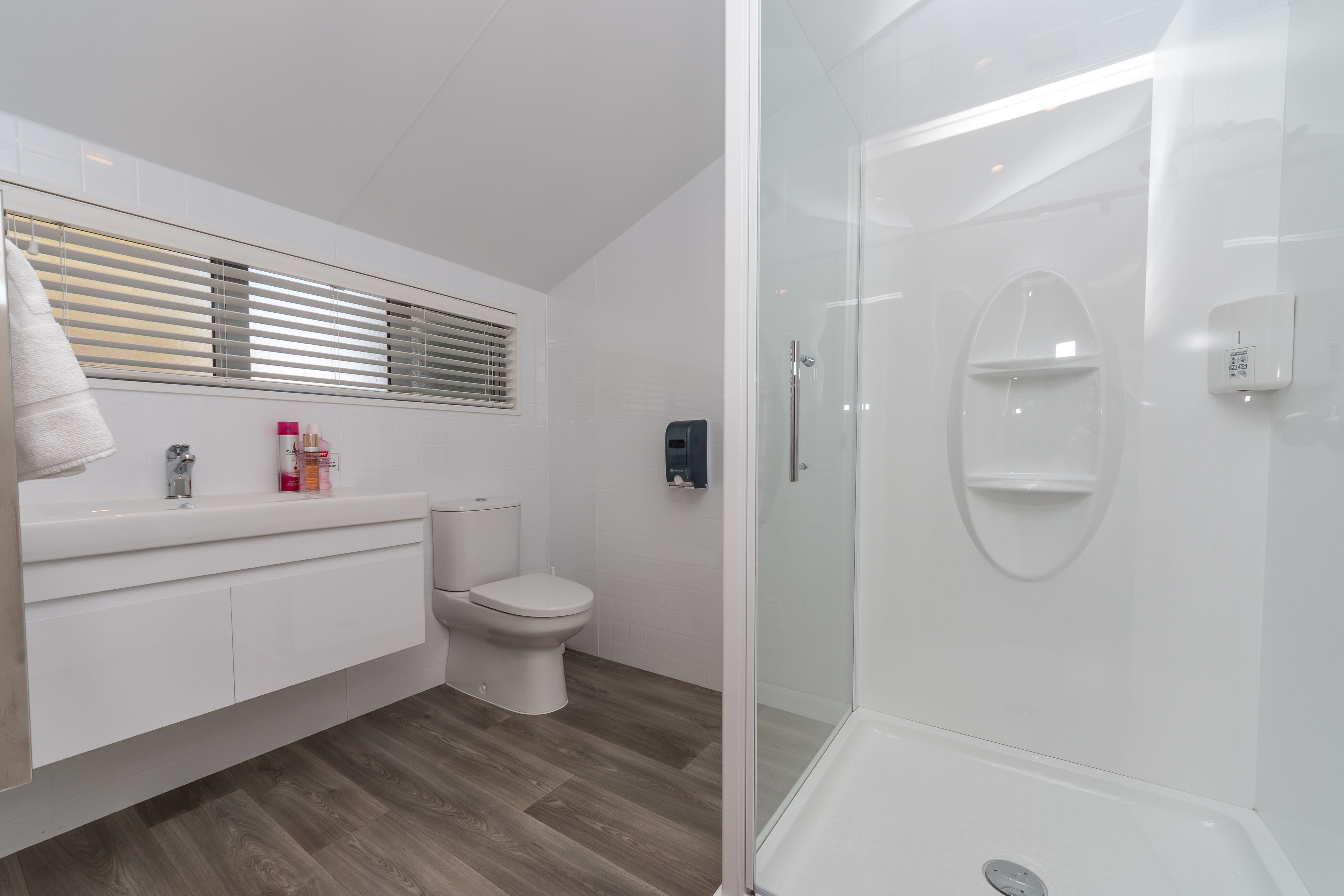 Un baño moderno con ducha de vidrio, inodoro blanco y tocador con espejo y espacio de almacenamiento.