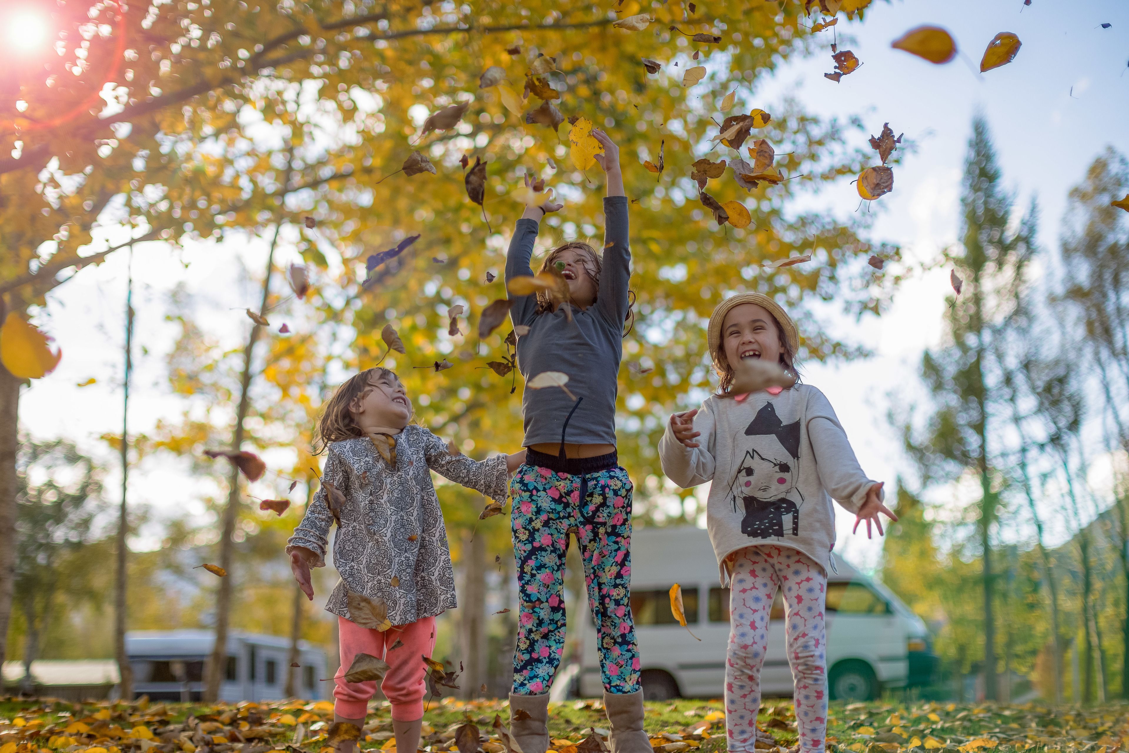 Three children playing in a park with trees and a vehicle in the background.