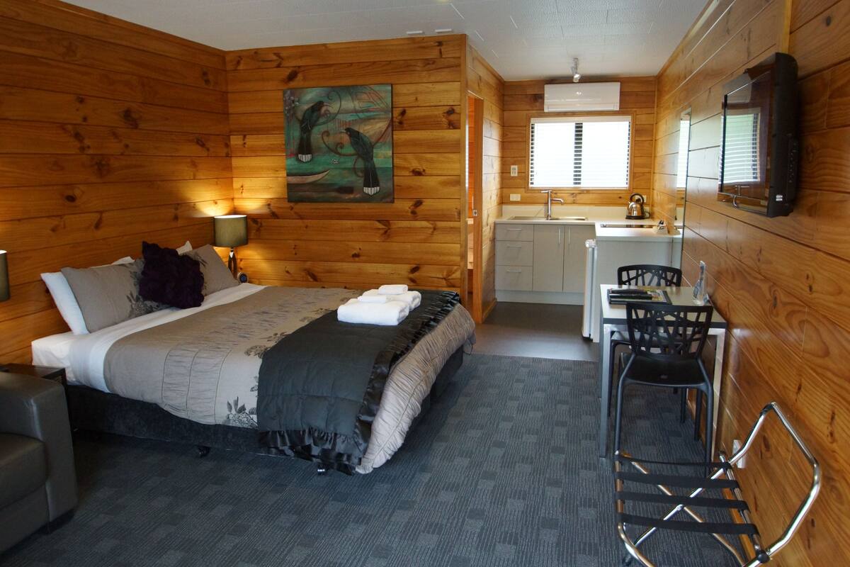 A wooden cabin-style room with a bed, a desk, and a kitchenette.