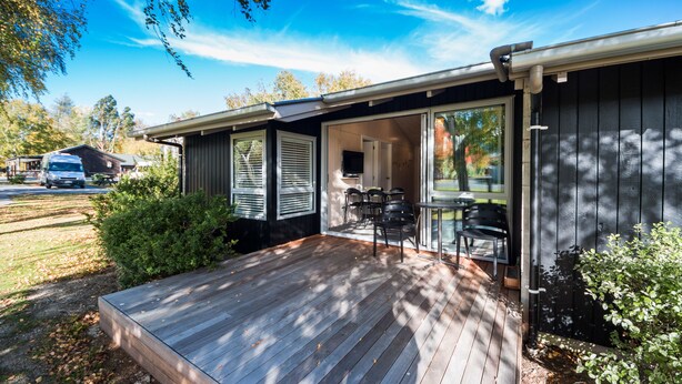 Een huis met een houten terras, een schuifdeur naar een patio met tuinmeubilair en een garage op de achtergrond.