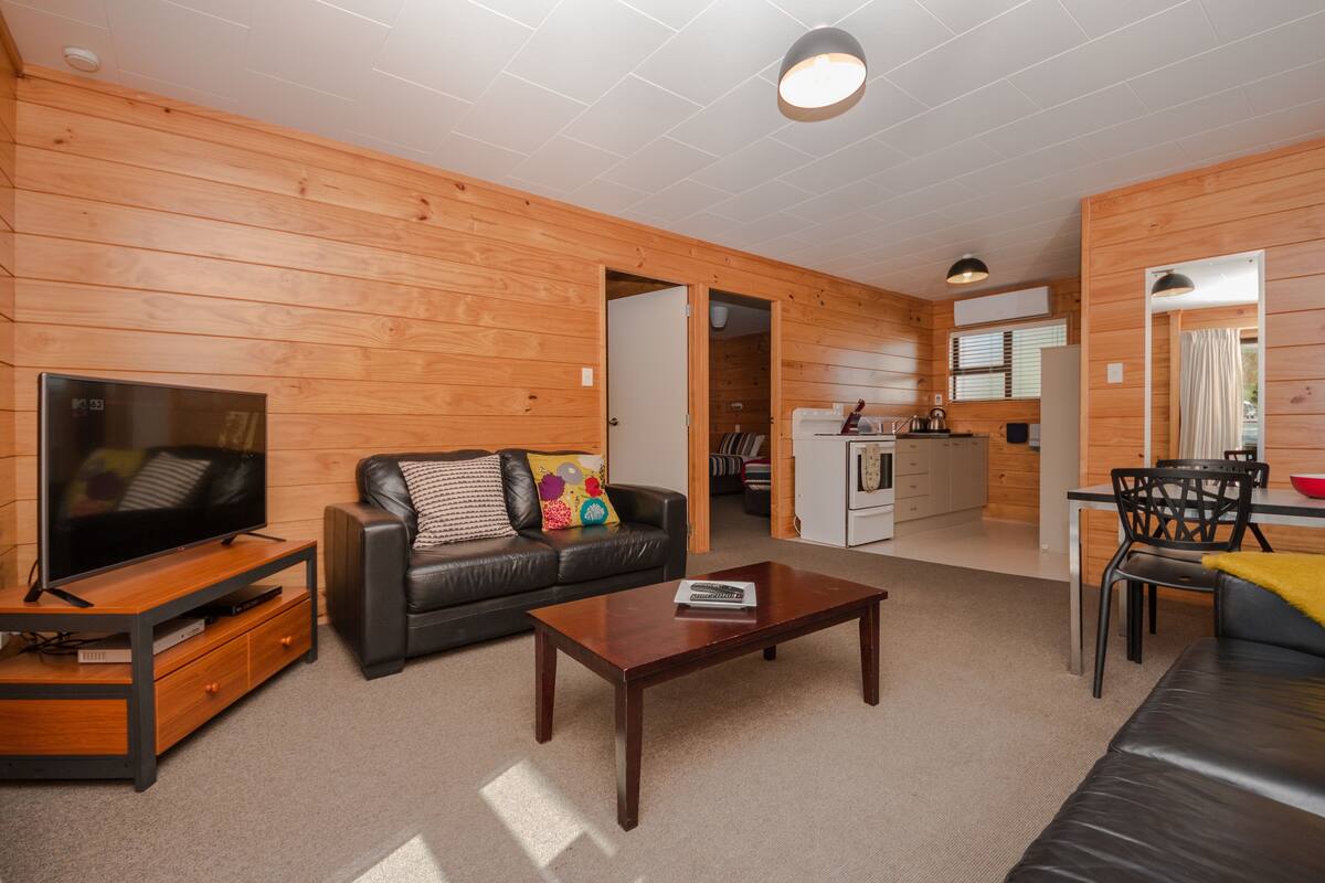 A modern living room with a TV, sofa, coffee table, and wooden walls.