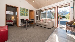 Een moderne woonkamer met een eethoek, een bank, een rode poef en uitzicht op buiten.